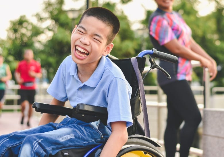 Asian child in wheelchair outside with a big smile on his face