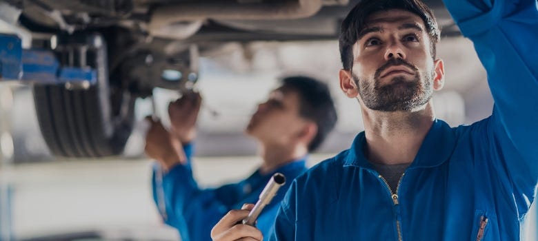 automotive service technician pointing under the hood of a vehicle